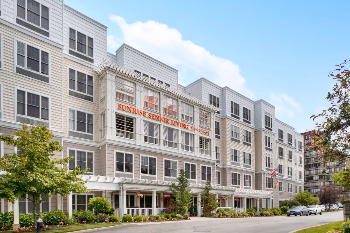 Front exterior of a multi-story Sunrise Senior Living facility with landscaped entrance and parked cars.