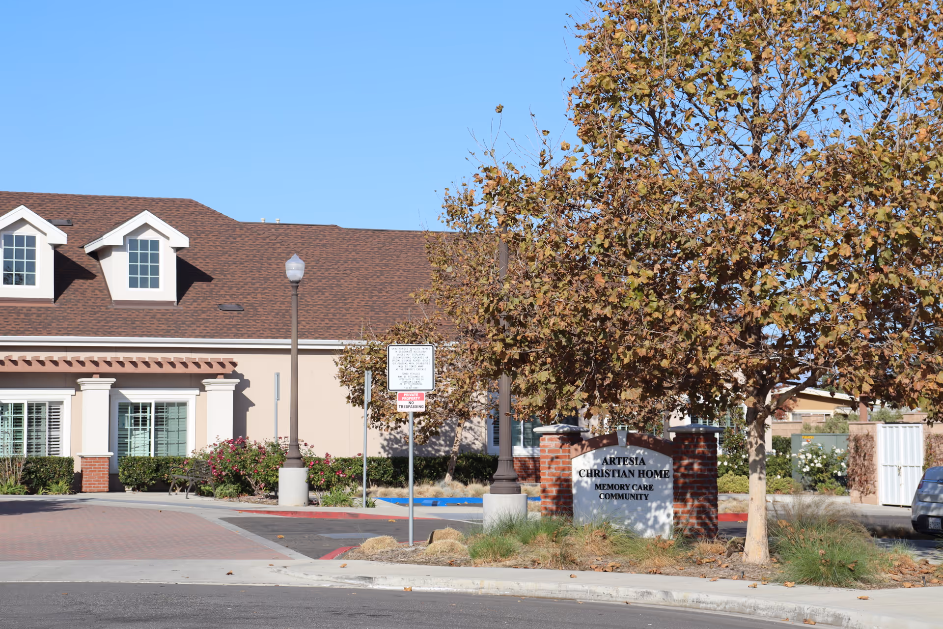 Front entrance of Artesia Christian Home Memory Care Community showing the brick sign, trees, and building facade.