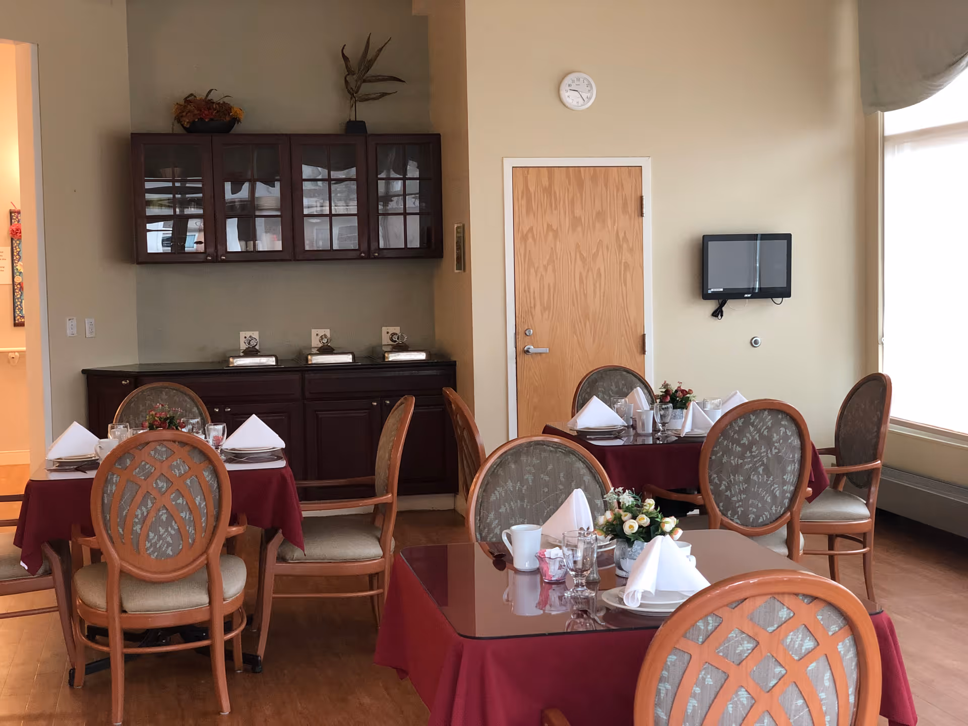 Dining room with several tables set with white napkins, floral centerpieces, and wooden chairs.