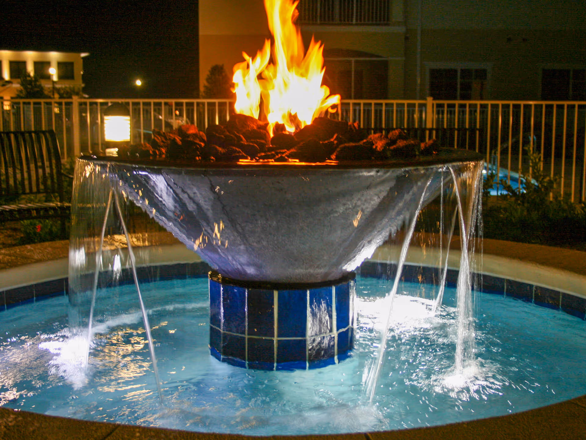 A nighttime outdoor fountain with cascading water and a bowl-shaped fire feature in the center.