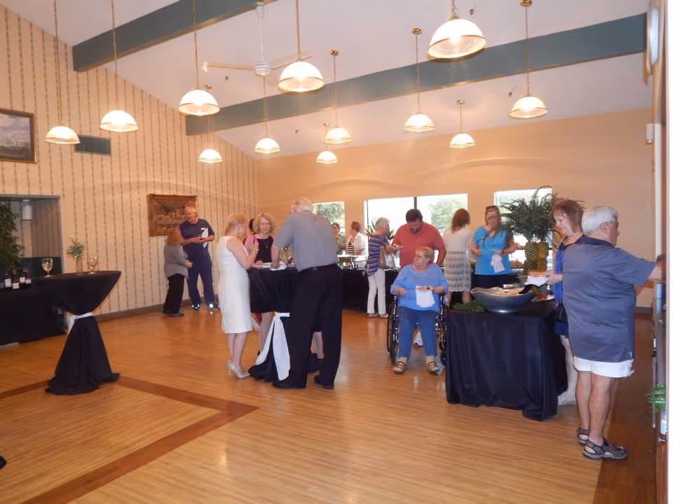 Seniors gathered in a communal dining/event room with buffet tables and hanging pendant lights.