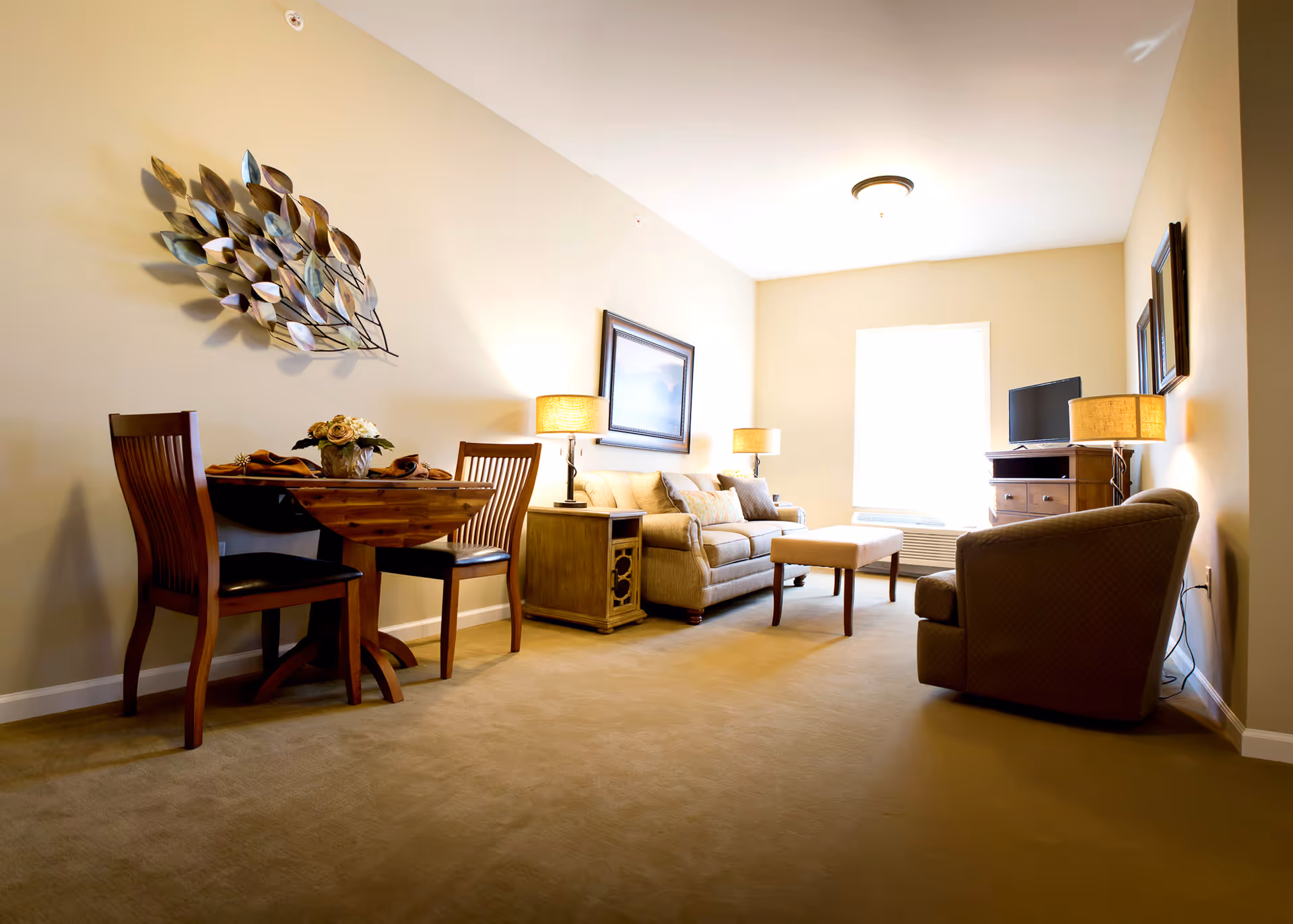 Well-lit living room with a sofa, armchair, coffee table, small dining table and decorative wall art.