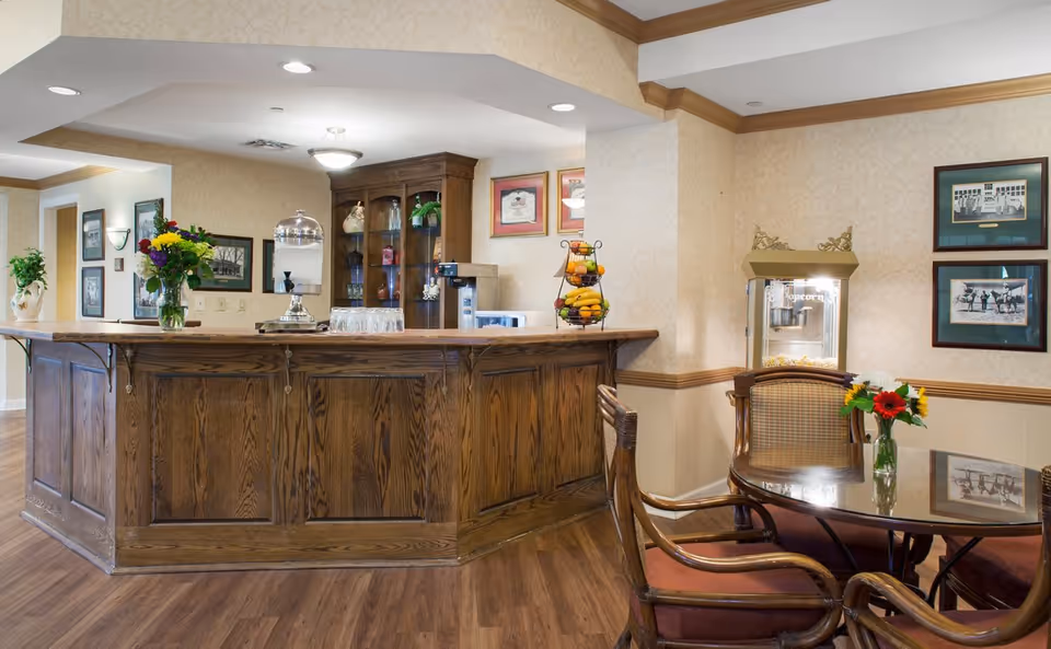 Wood-paneled service counter and seating area in a senior living common room with flowers and a popcorn machine.