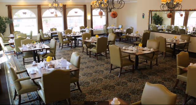 Spacious dining room with multiple set tables, green upholstered chairs, chandeliers, and large arched windows.