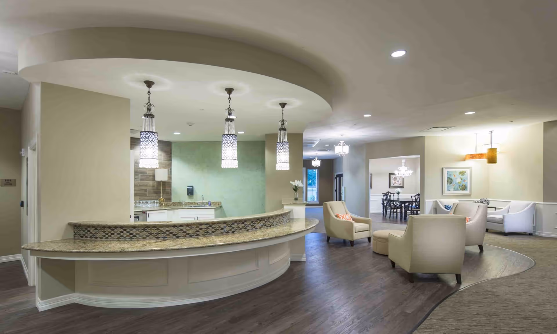Open reception and lounge area with a curved front desk, hanging pendant lights, and several armchairs near a dining space.