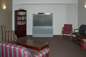 Common lounge area with upholstered sofas and chairs, a large television on a stand, and a bookshelf.
