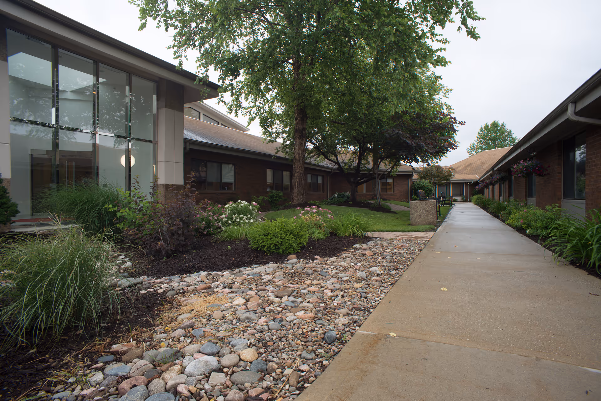 Walkway and landscaped courtyard between single-story brick buildings with trees and windows.