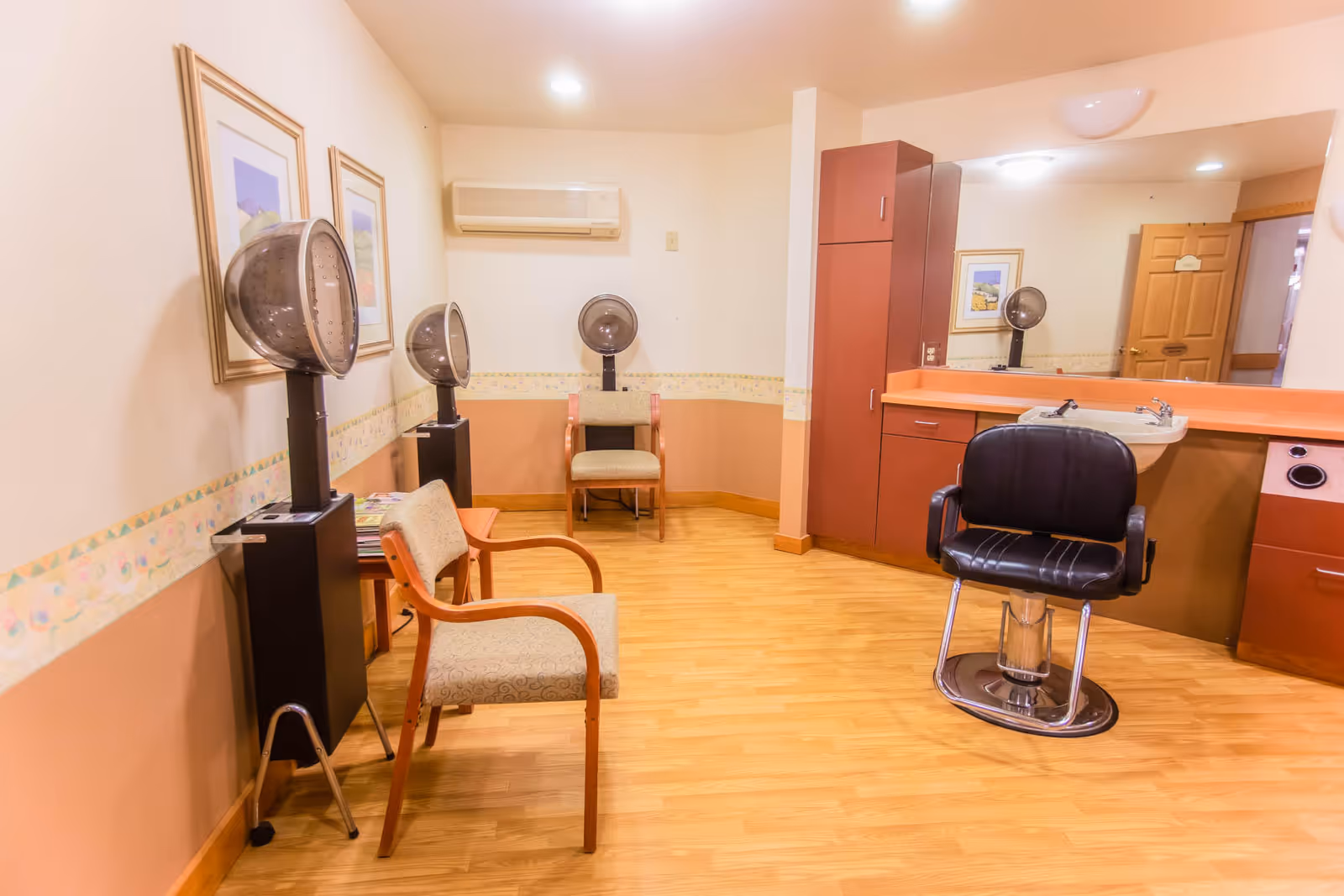 Interior salon area with styling chairs, hooded hair dryers, a wash sink, mirrors and waiting chairs in a warm-toned room.
