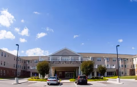 Senior living facility exterior with entrance canopy and parked cars.