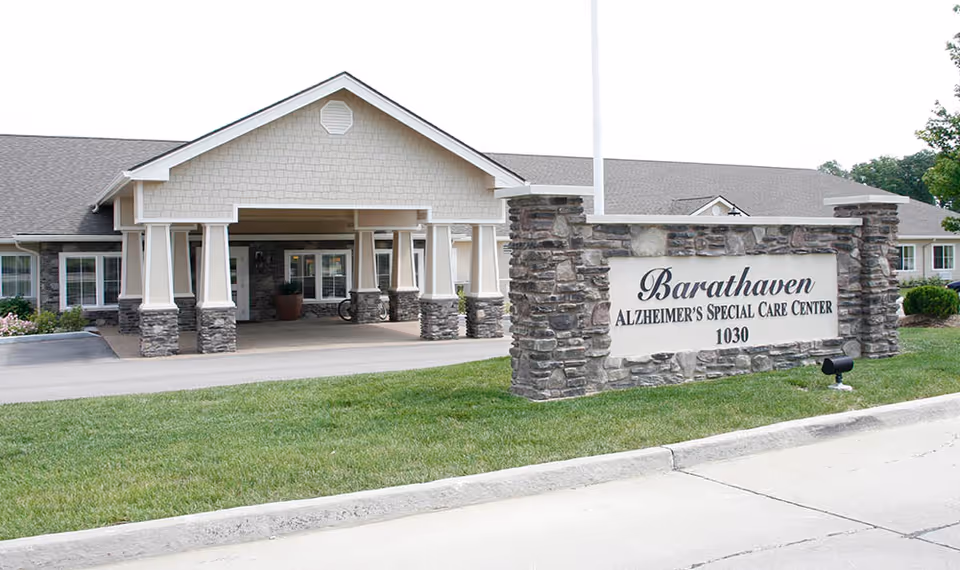 Exterior view of Barathaven Alzheimer's Special Care Center showing the entrance with a covered driveway supported by stone and white pillars, and a stone sign in front displaying the facility's name and address number 1030.