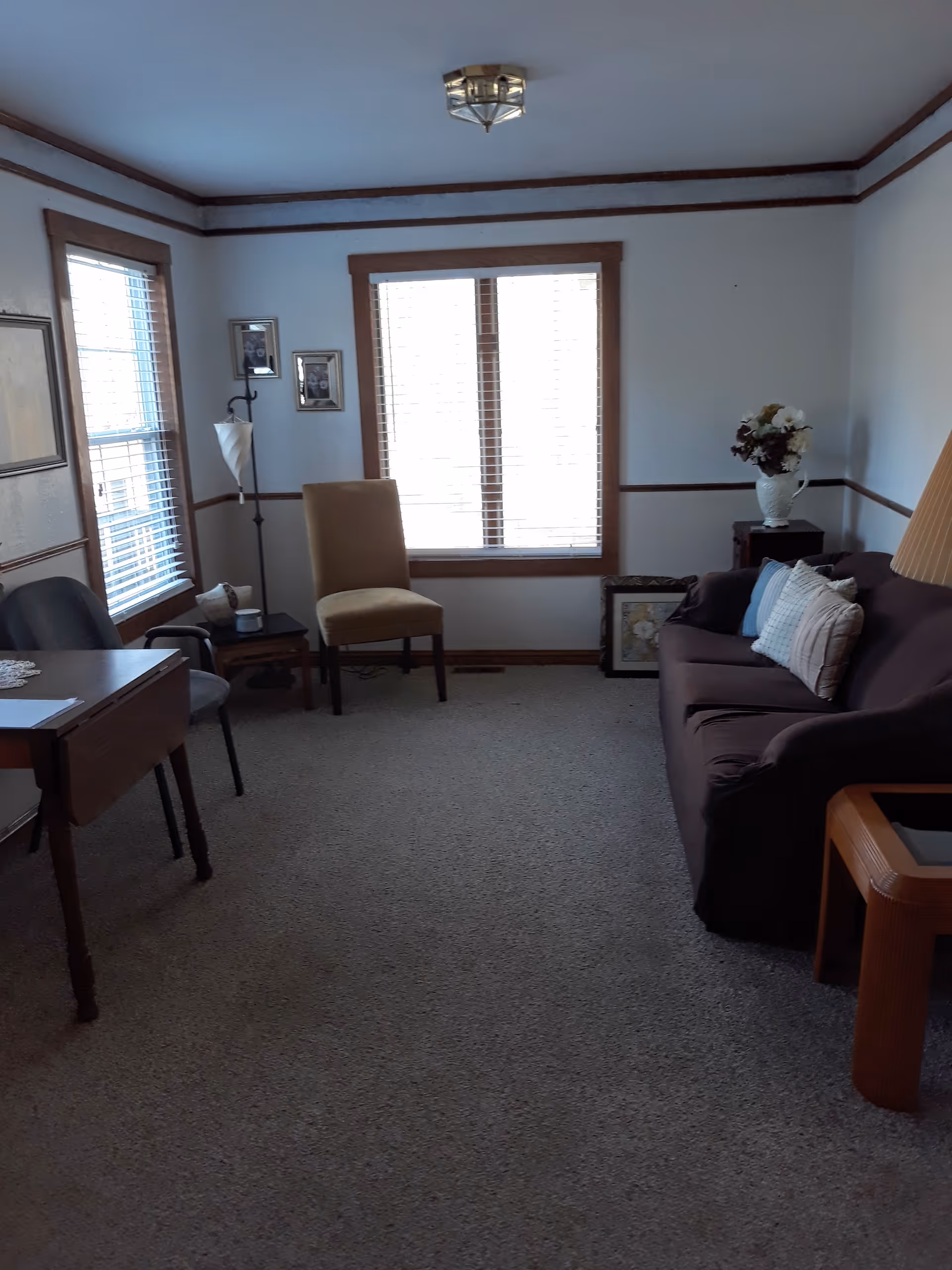Small living room with a sofa, chairs, side tables, and a window with blinds.