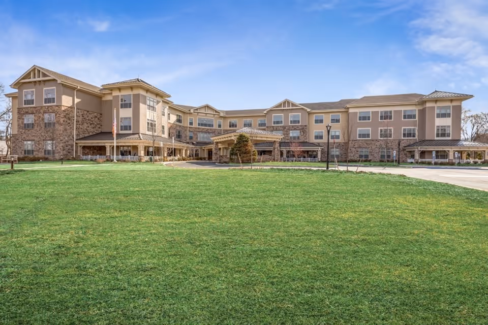 Front exterior of a three-story senior living building with a large green lawn and a covered main entrance.