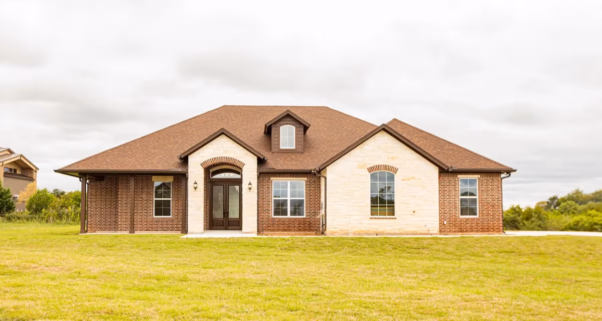 Front exterior of a single-story brick-and-stone senior living building with a grassy lawn.