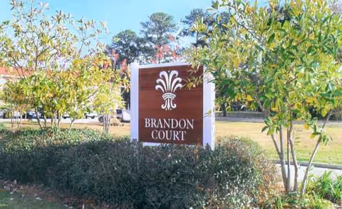Front exterior view of Brandon Court Nursing sign amid shrubs and trees in daylight