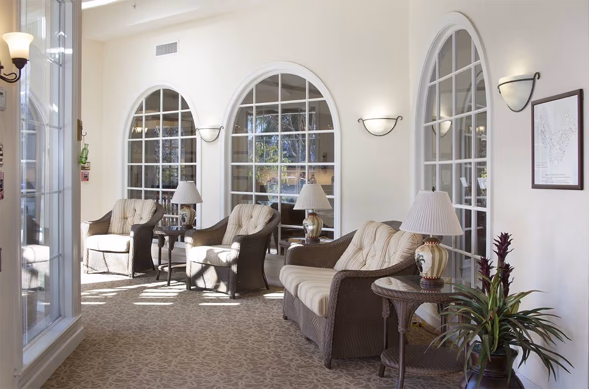 Bright lounge with wicker armchairs, side tables, and lamps arranged in front of arched windows.