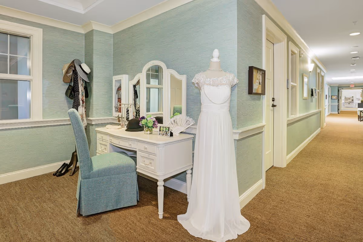 A softly lit interior corridor vignette with a white vanity and chair beside a mannequin dressed in a white gown.