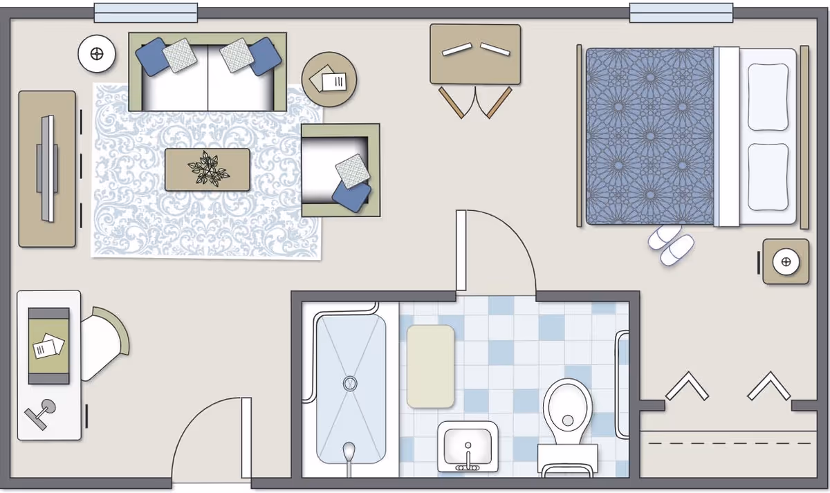 Top-down floor plan of a senior living unit at Lakewood Place showing a living room with sofa, armchair, coffee table, TV, and desk; a bedroom with a bed, nightstand, slippers, and a small table with two chairs; and a bathroom with a bathtub, sink, toilet, and a small bench.