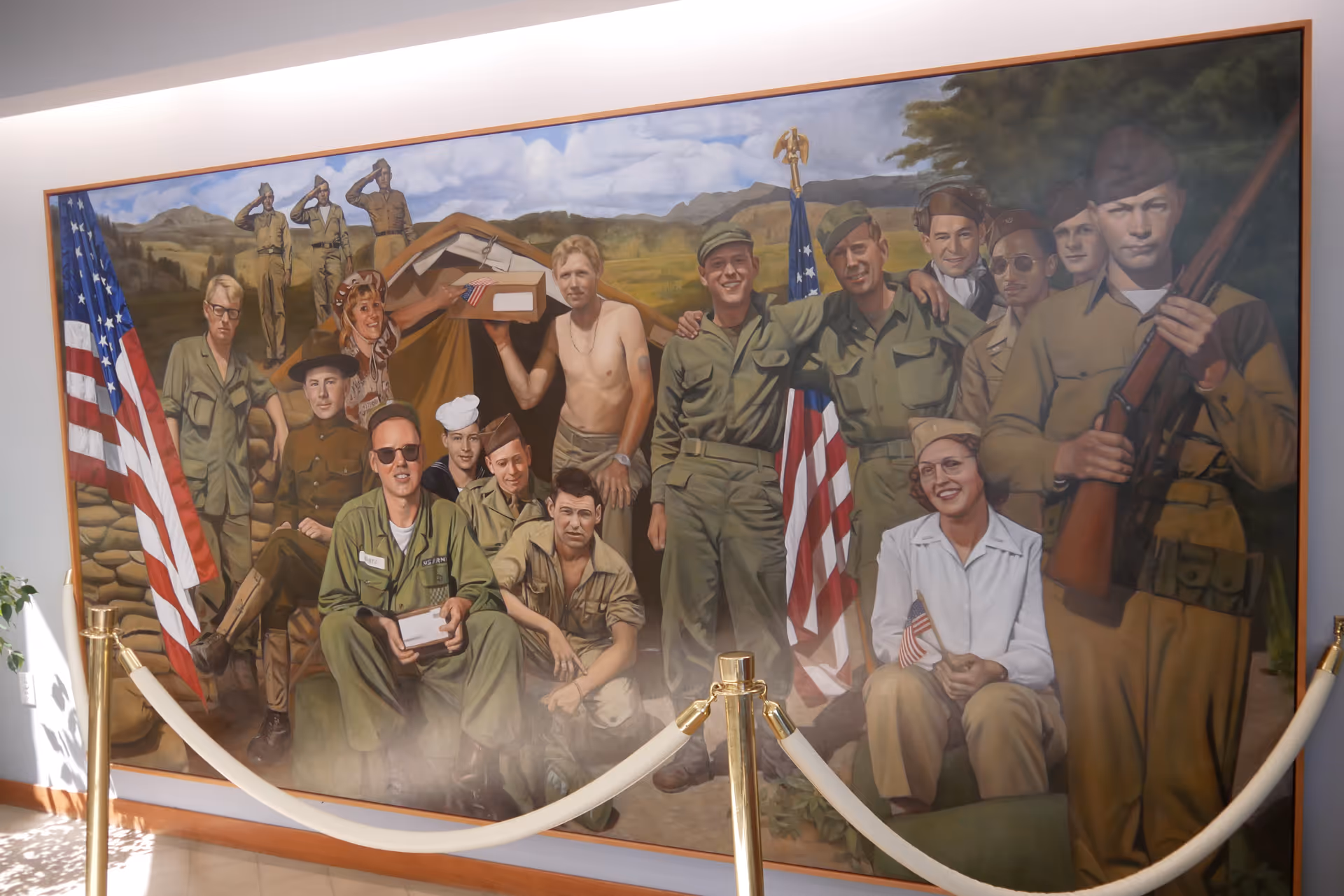 Mural painting of World War II-era servicemembers and a nurse with American flags displayed on an interior wall behind stanchions.