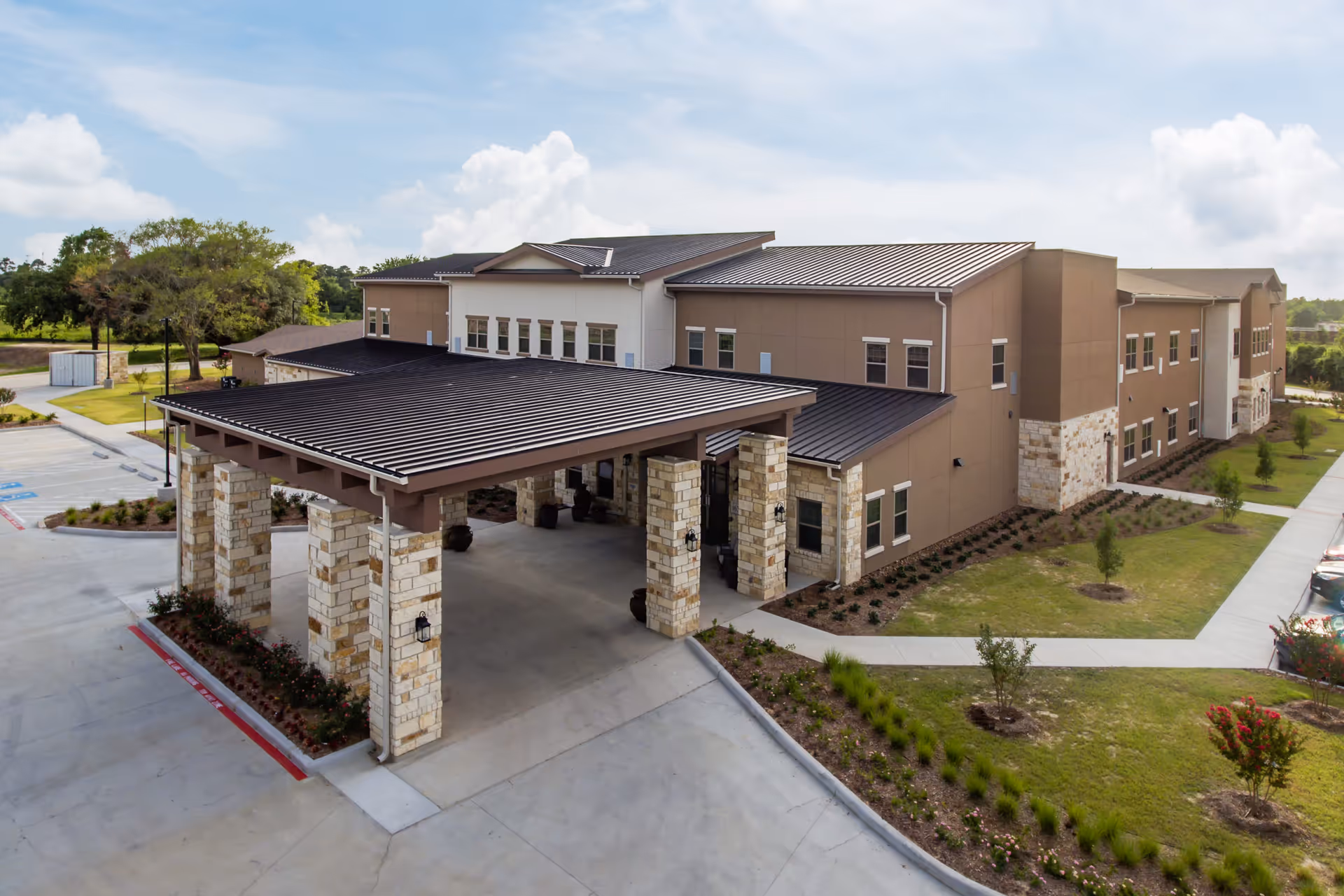 Exterior front entrance of a two-story senior living facility with a covered porte-cochere and landscaped grounds.