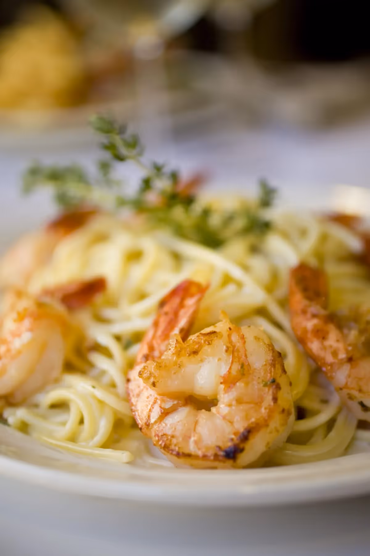 Close-up of a plate of spaghetti pasta topped with grilled shrimp and garnished with a sprig of fresh herbs.