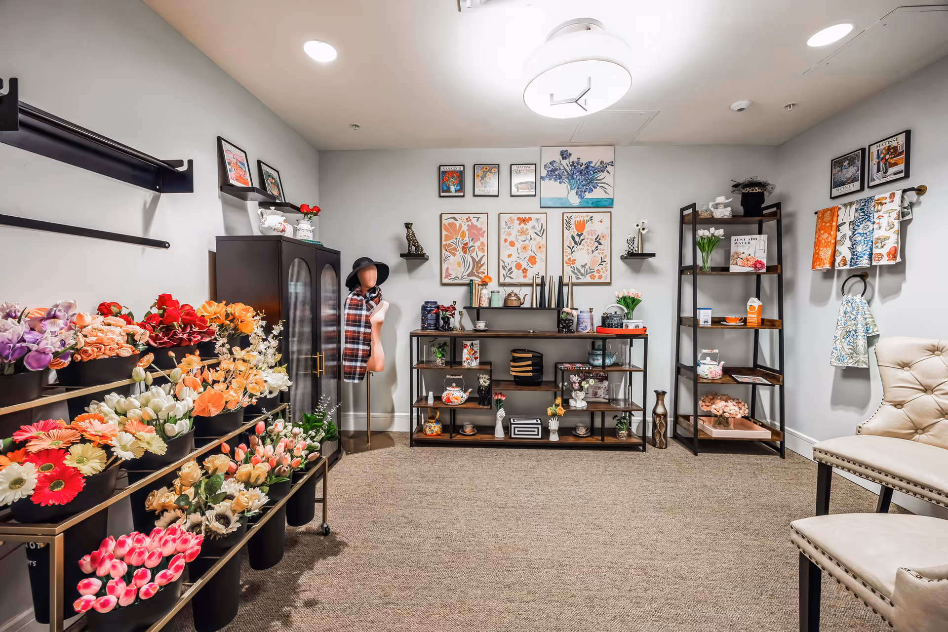 Interior boutique-style room with racks of colorful artificial flowers, shelving with decorative items and a mannequin, and seating.
