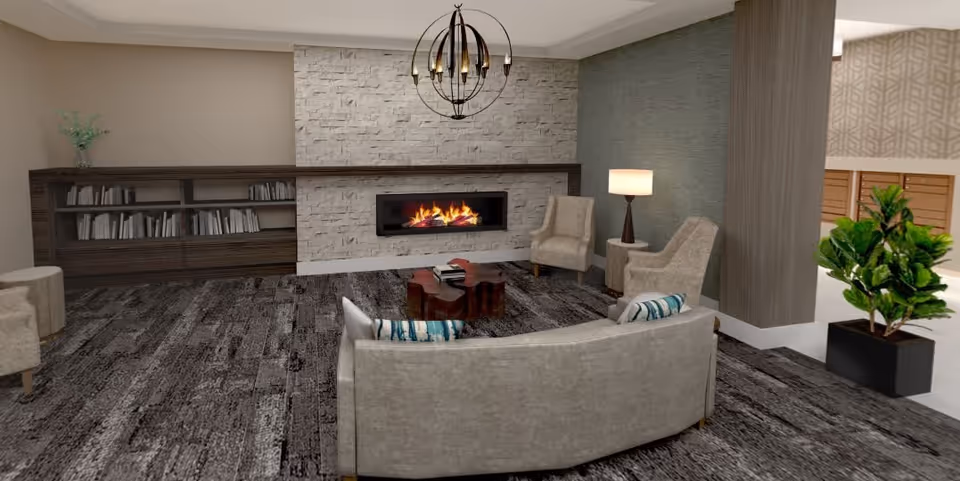 A cozy living room area featuring a modern stone fireplace with a burning fire, a curved beige sofa with patterned pillows, two beige armchairs, a wooden coffee table, a floor lamp, a bookshelf filled with books, and a potted plant near a wooden column.