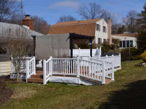 White wooden deck with stairs and railing extends from a residential house onto a green lawn.
