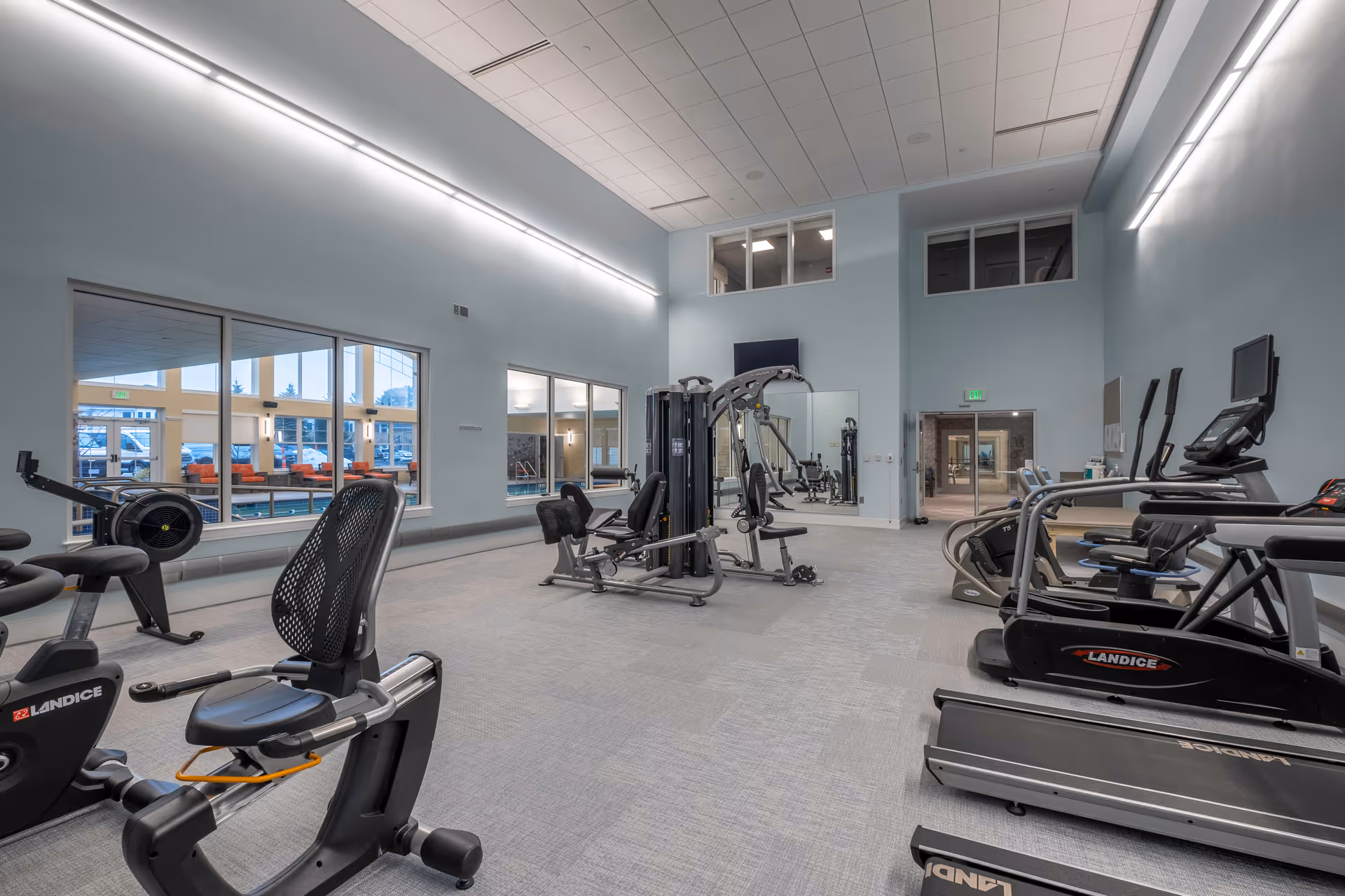 Spacious fitness room with treadmills, exercise bikes, strength machines, and large windows overlooking an indoor pool.