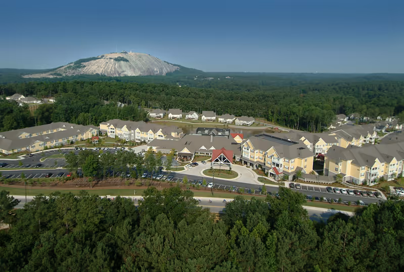 Aerial view of Park Springs senior living facility surrounded by trees with a large rocky mountain in the background under a clear blue sky.