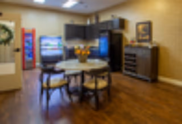 Round dining table with four chairs in a communal room featuring a kitchenette, refrigerator and vending machine.