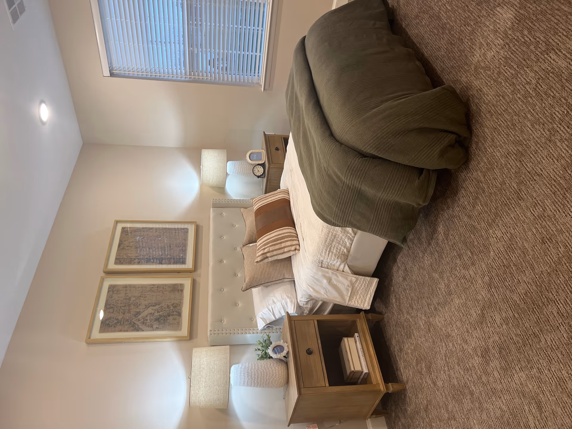A tidy bedroom with a bed topped by pillows and a green throw, two nightstands with lamps, and framed artwork on the wall.