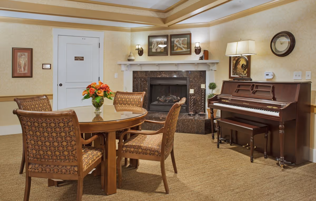 Cozy common room with a round table and chairs, a fireplace, and an upright piano.