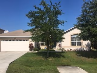 Front view of a single-story beige senior living facility with a driveway and trees.