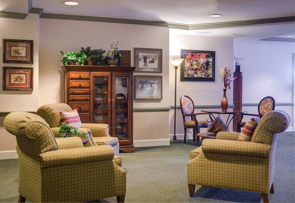 Cozy lounge area with patterned upholstered armchairs facing each other, a wooden cabinet, framed artwork, and a small table with chairs.