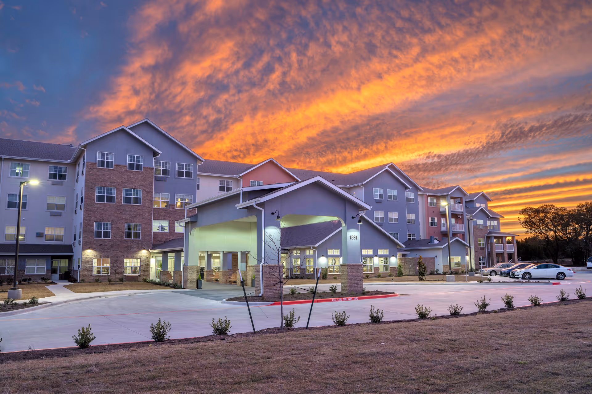 Exterior front view of a multi-story senior living facility at sunset with a dramatic orange sky.