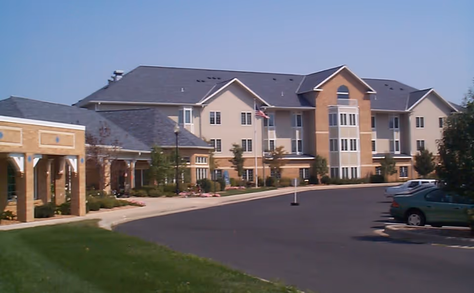 Front exterior of a multi-story senior living community building with a driveway and parked cars.