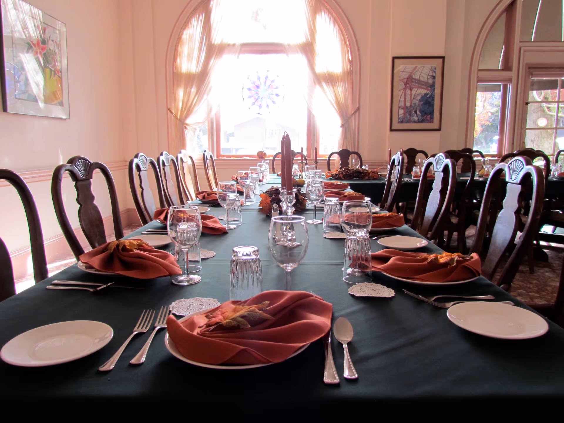Long dining table in an elegant dining room set with place settings, glassware, and folded napkins in front of arched windows.