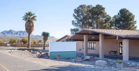 Desert landscape in front of a beige senior living center with a covered entrance and mountains.