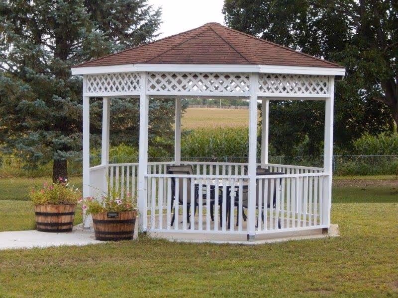 White wooden gazebo with a table and chairs on a grassy lawn and two wooden planters nearby.