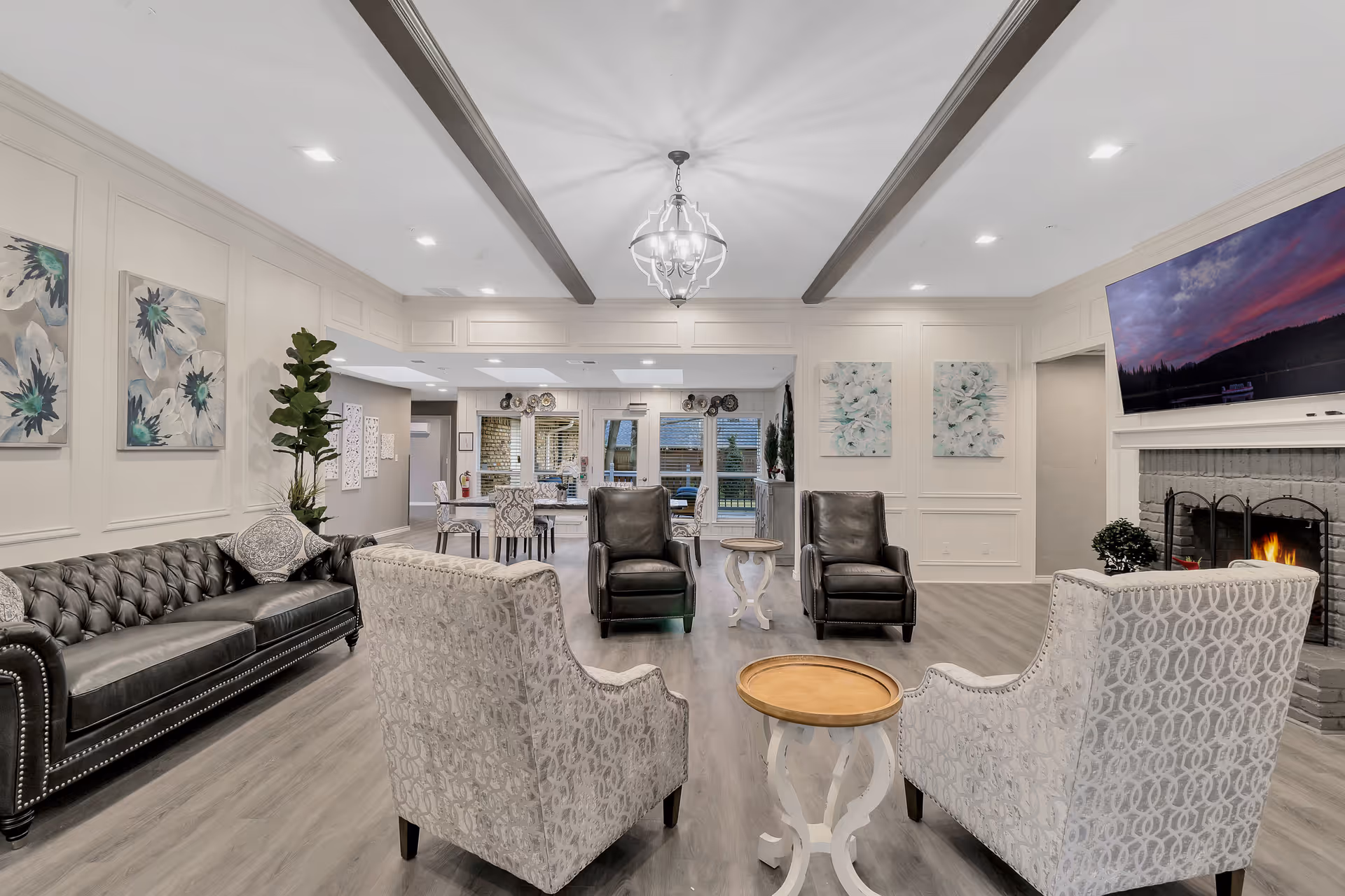 Spacious, elegantly furnished common living room with sofas and armchairs arranged around small tables, a fireplace, and a wall-mounted TV.