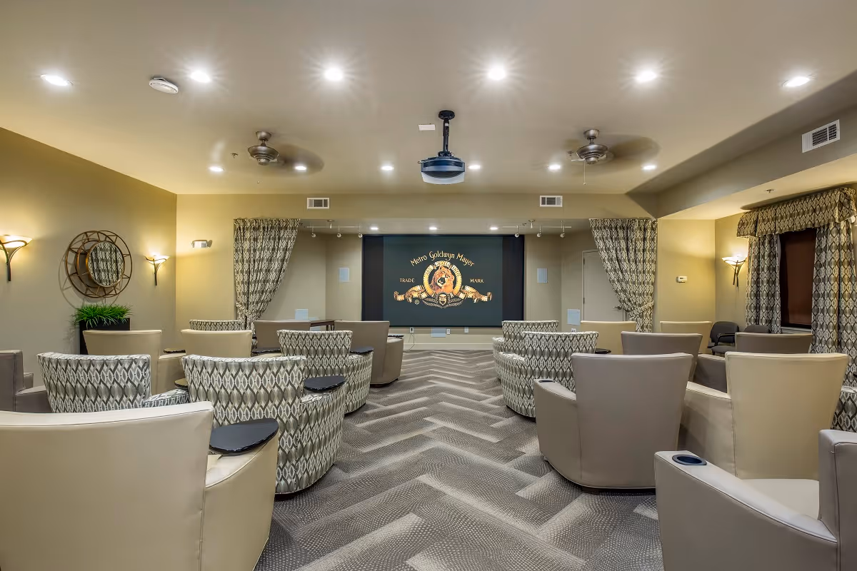 A comfortable media/theater room with upholstered armchairs arranged facing a projection screen showing a Metro Goldwyn Mayer logo.