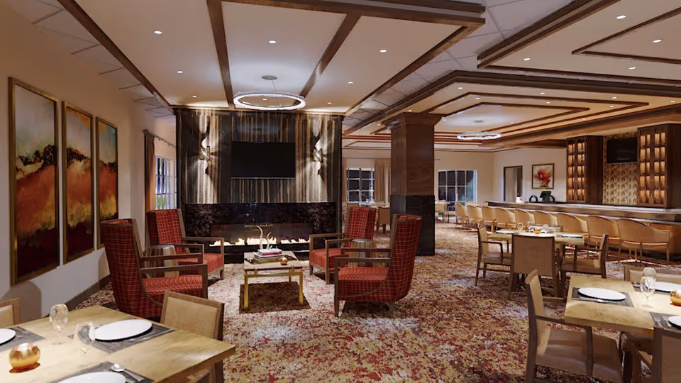 A spacious and elegantly decorated common area featuring a seating arrangement with red cushioned chairs around a coffee table in front of a modern fireplace and a mounted flat-screen TV. The room has a patterned carpet, wooden ceiling beams, and multiple dining tables set with plates, glasses, and cutlery. The background includes a bar area with stools and additional seating.