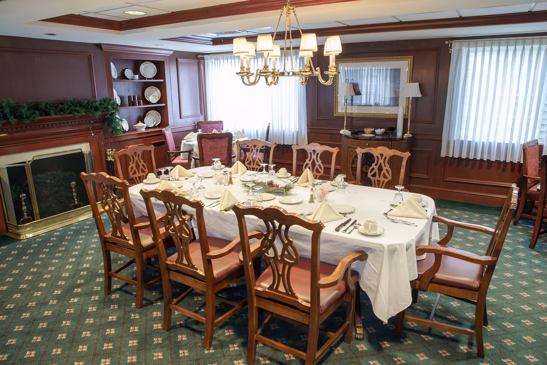 Formal dining room with a long table set for a meal, wooden chairs, chandelier, fireplace and paneled walls.