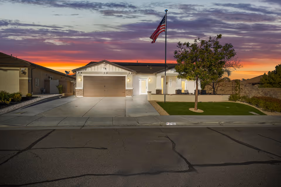 Front exterior of Betty's Place Assisted Living in Murrieta, a single-story building with a two-car garage, flagpole, and a small lawn at sunset.
