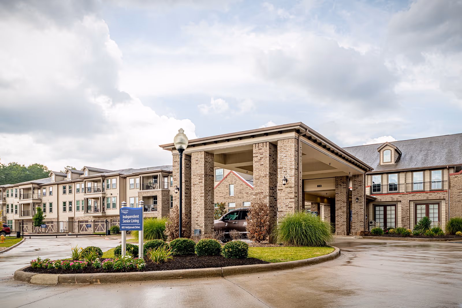 Front entrance of Parkview on Hollybrook senior living building with a covered porte-cochere, landscaped roundabout, and driveway.