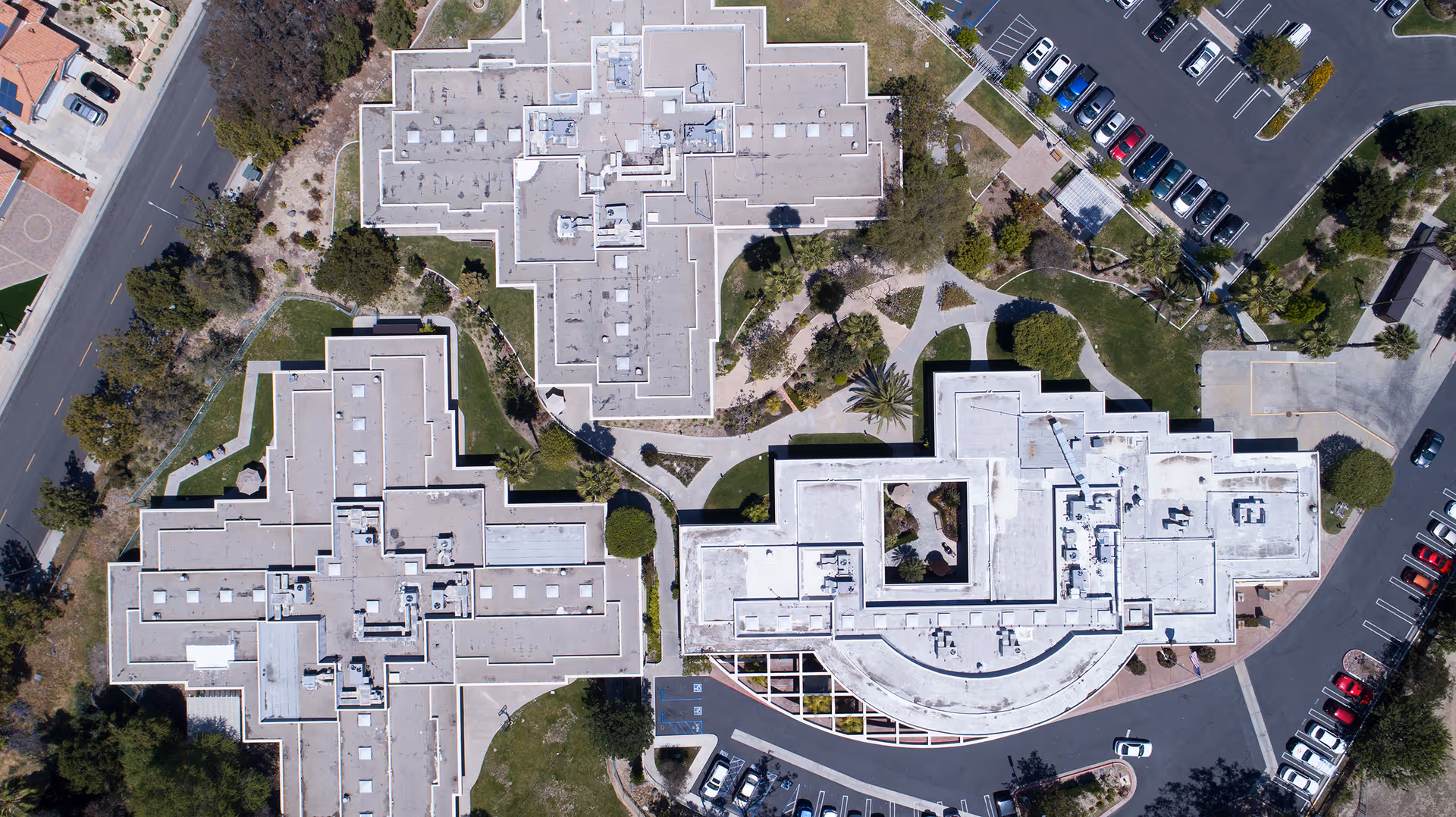 Aerial view of Vista Knoll Specialized Care facility showing three large building structures with flat roofs, surrounded by parking lots, roads, and landscaped green areas with trees and pathways.