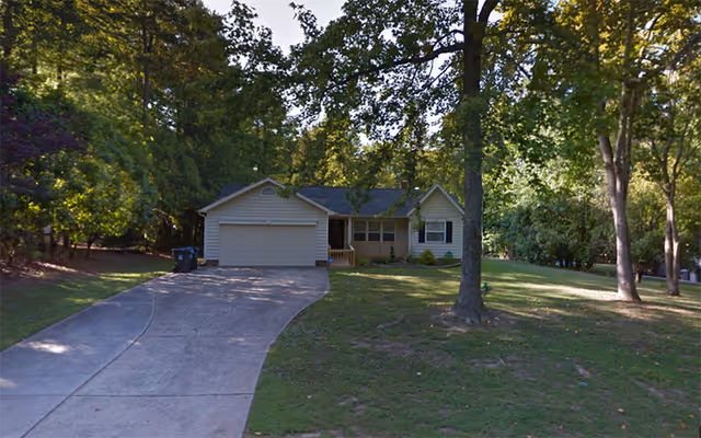 Single-story house with an attached two-car garage, driveway, and tree-filled front yard.