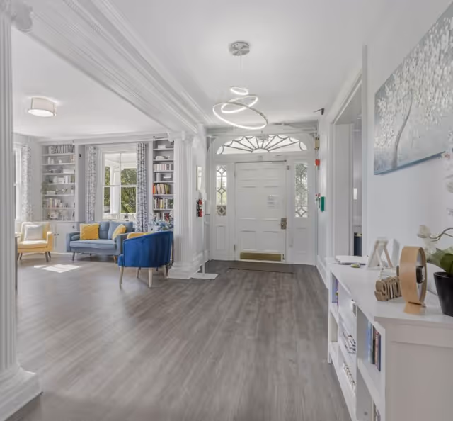 Bright senior living entrance lobby with white columns, seating area, bookshelves, and double front doors.