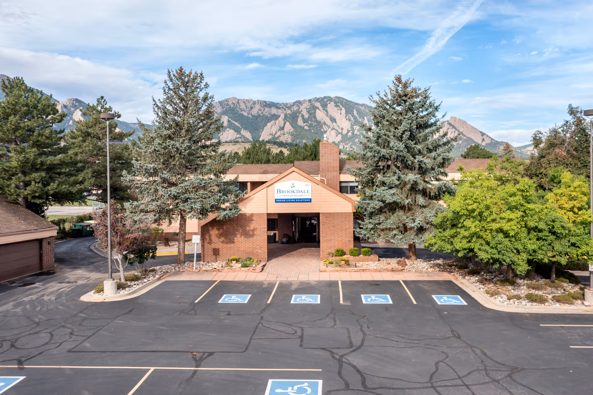 Front exterior of the Brookdale Meridian Boulder building with a parking lot, marked handicapped spaces, trees, and mountains in the background.