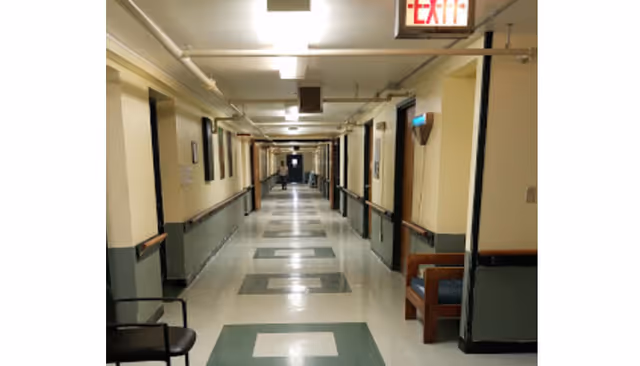 Long well-lit interior hallway with tiled floor, handrails and seating along the walls and an EXIT sign overhead.